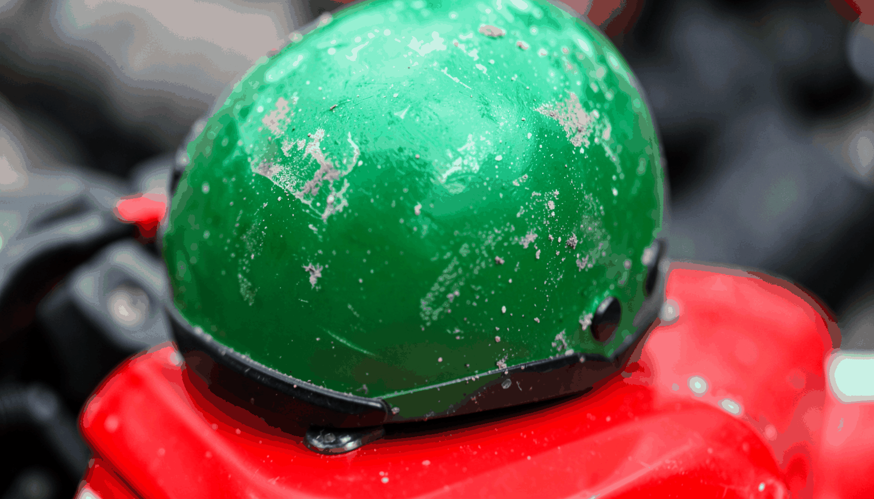 Close-up helm ojek online berwarna hijau tergeletak di atas motor, tekstur permukaan helm yang tergores dan berdebu