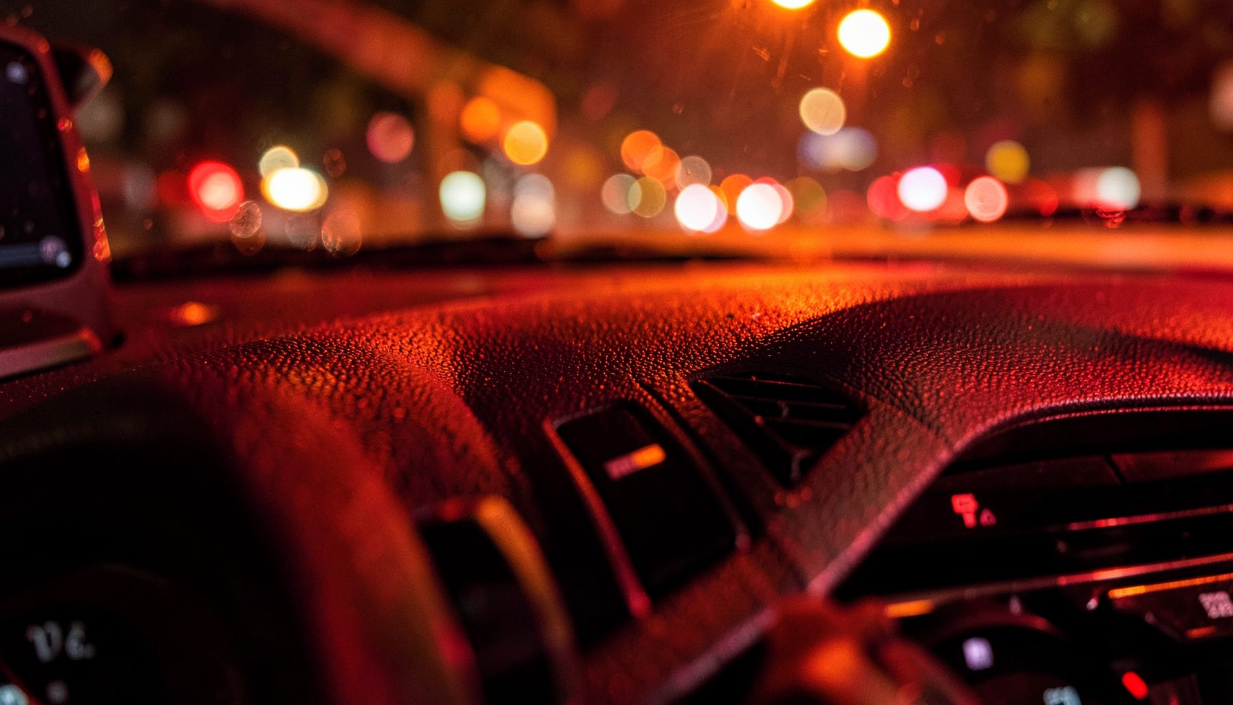 Tekstur close-up dashboard kendaraan dengan refleksi cahaya jingga dari lampu jalan, suasana berkendara malam hari