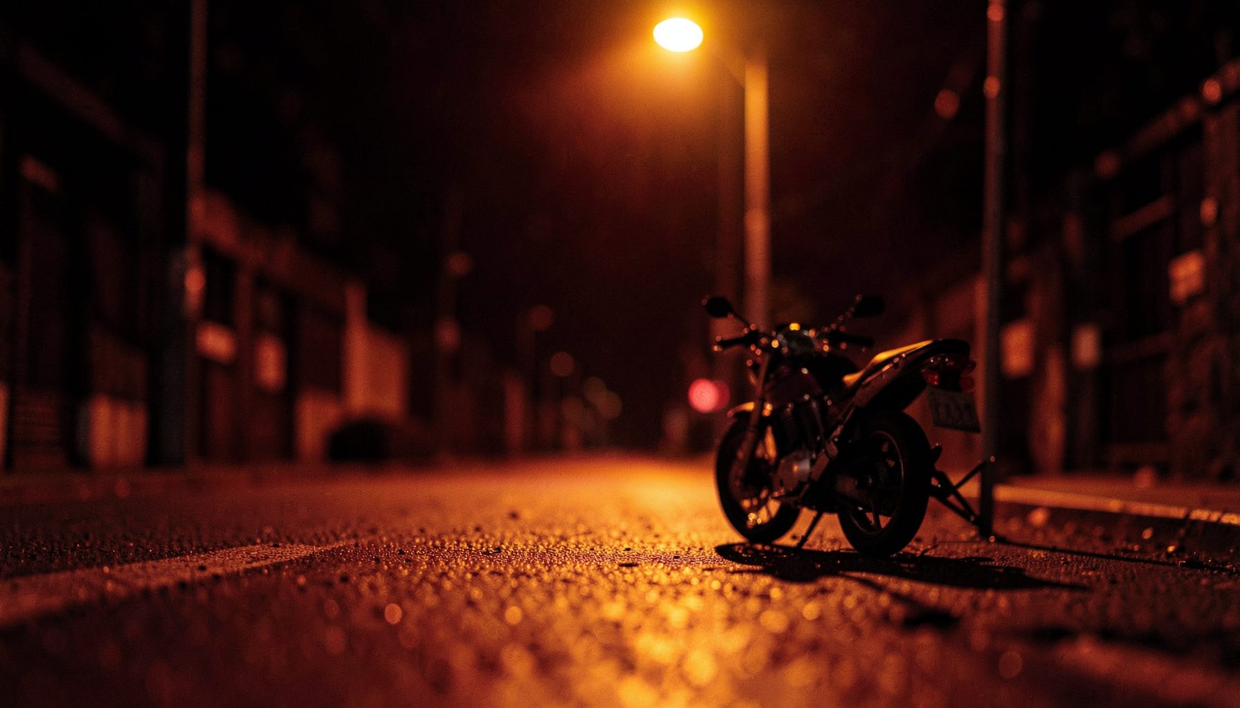 Jalanan malam yang sepi dengan satu kendaraan roda dua terparkir di bawah lampu jalan kuning, suasana mencekam