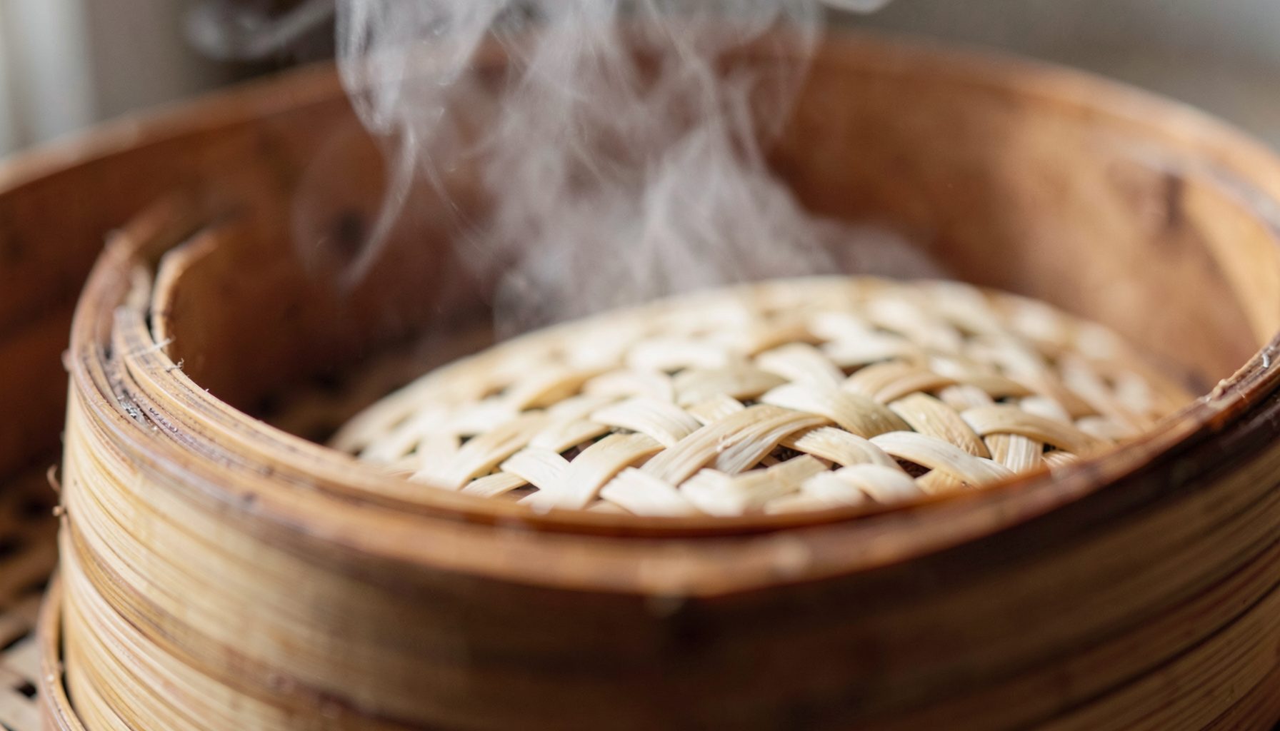 Extreme close-up of textured woven bamboo steamer with wisps of steam rising, soft natural light, earthy brown and cream tones